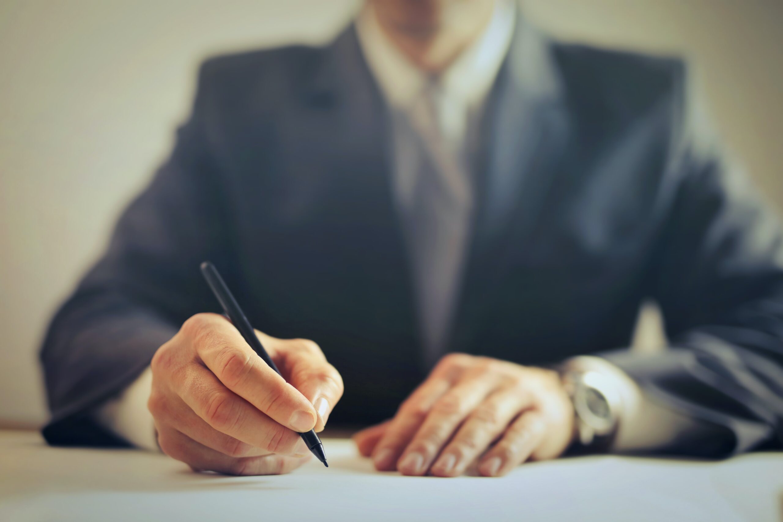 Mann im Anzug hält einen Stift in seiner Hand und schreibt auf ein Blatt Papier